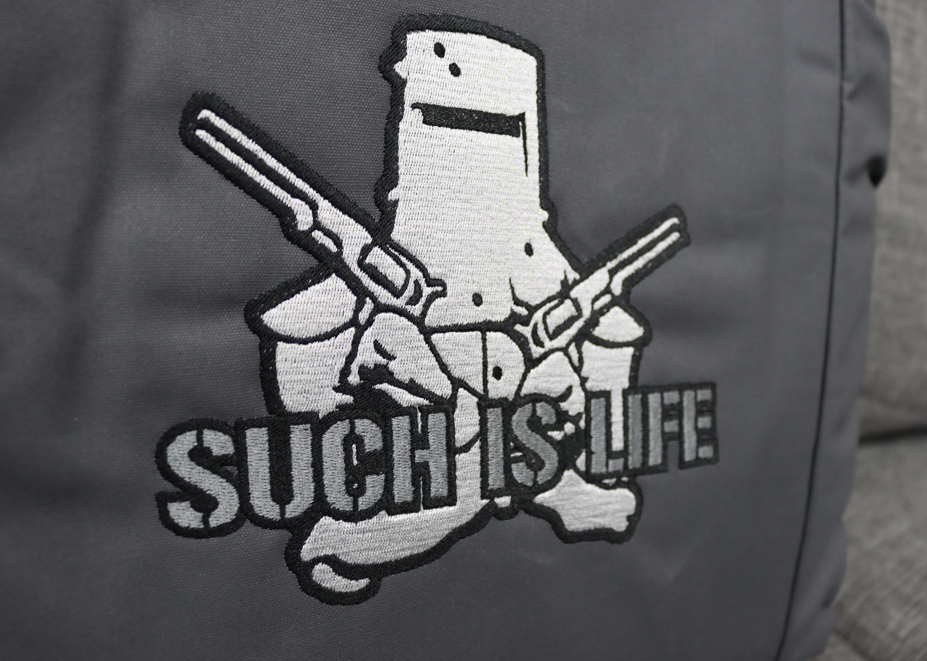 Close up of a grey canvas seat cover with a detailed black and white embroidery of Ned Kelly and the text "such is life"